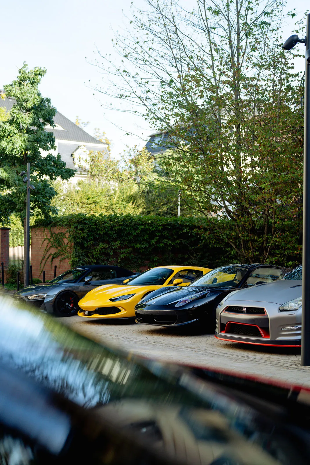 Vier Sportwagen parken nebeneinander in einem Hof, darunter ein gelber Ferrari und ein grauer Nissan GT-R