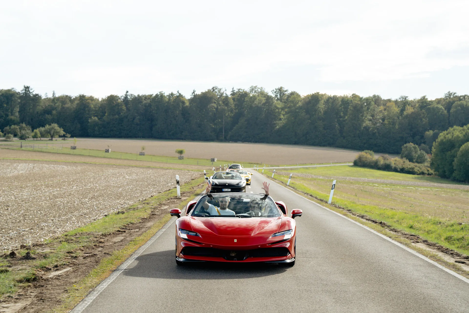 Roter Ferrari führt einen Konvoi bei einer der Sportwagenausfahrten von EPICO Circle über eine Landstraße, die Insassen winken