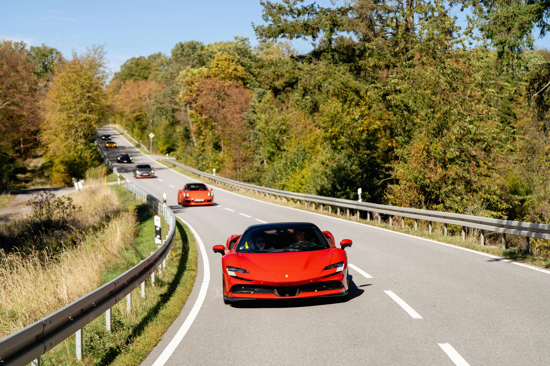 Roter Ferrari und weitere Sportwagen im Konvoi auf einer Landstraße im Herbstwald bei einer EPICO Circle Sportwagentour